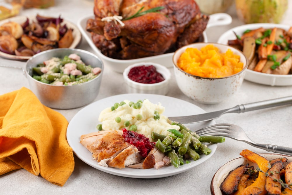 A Thanksgiving meal with sliced turkey, green beans, mashed potatoes, cranberry sauce, and a roasted turkey.